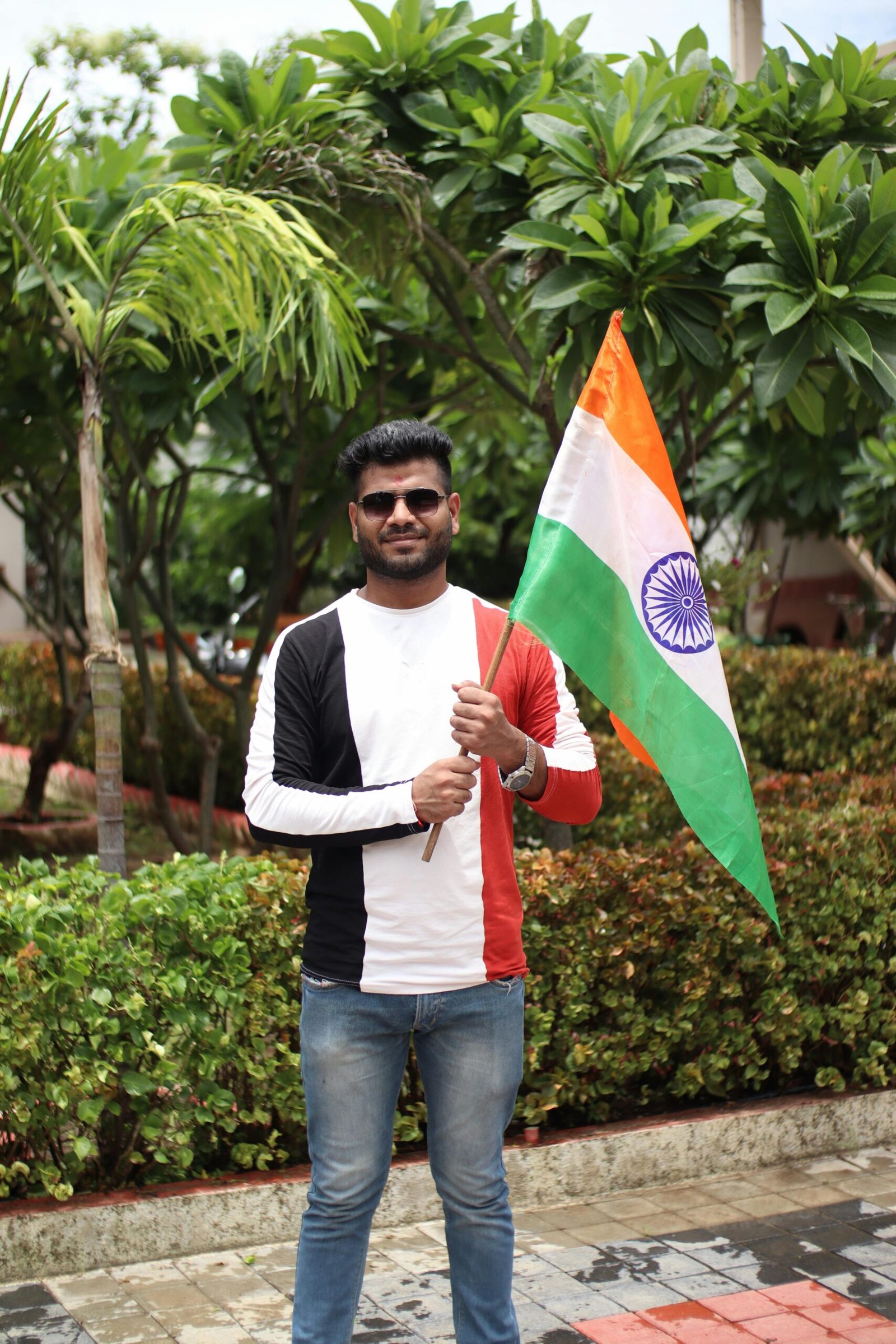 South Asian man celebrating with Indian national flag in a sunny outdoor setting.