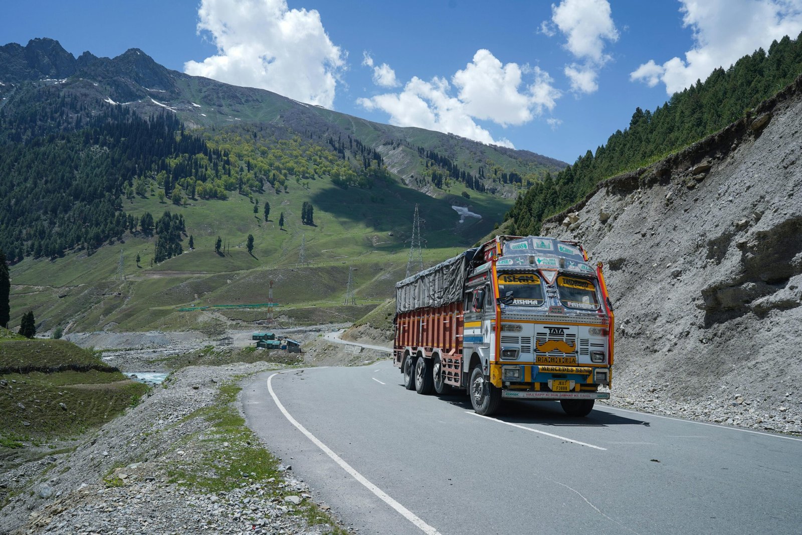 A vibrant truck travels through the breathtaking landscapes of Kashmir on the NH1 highway.